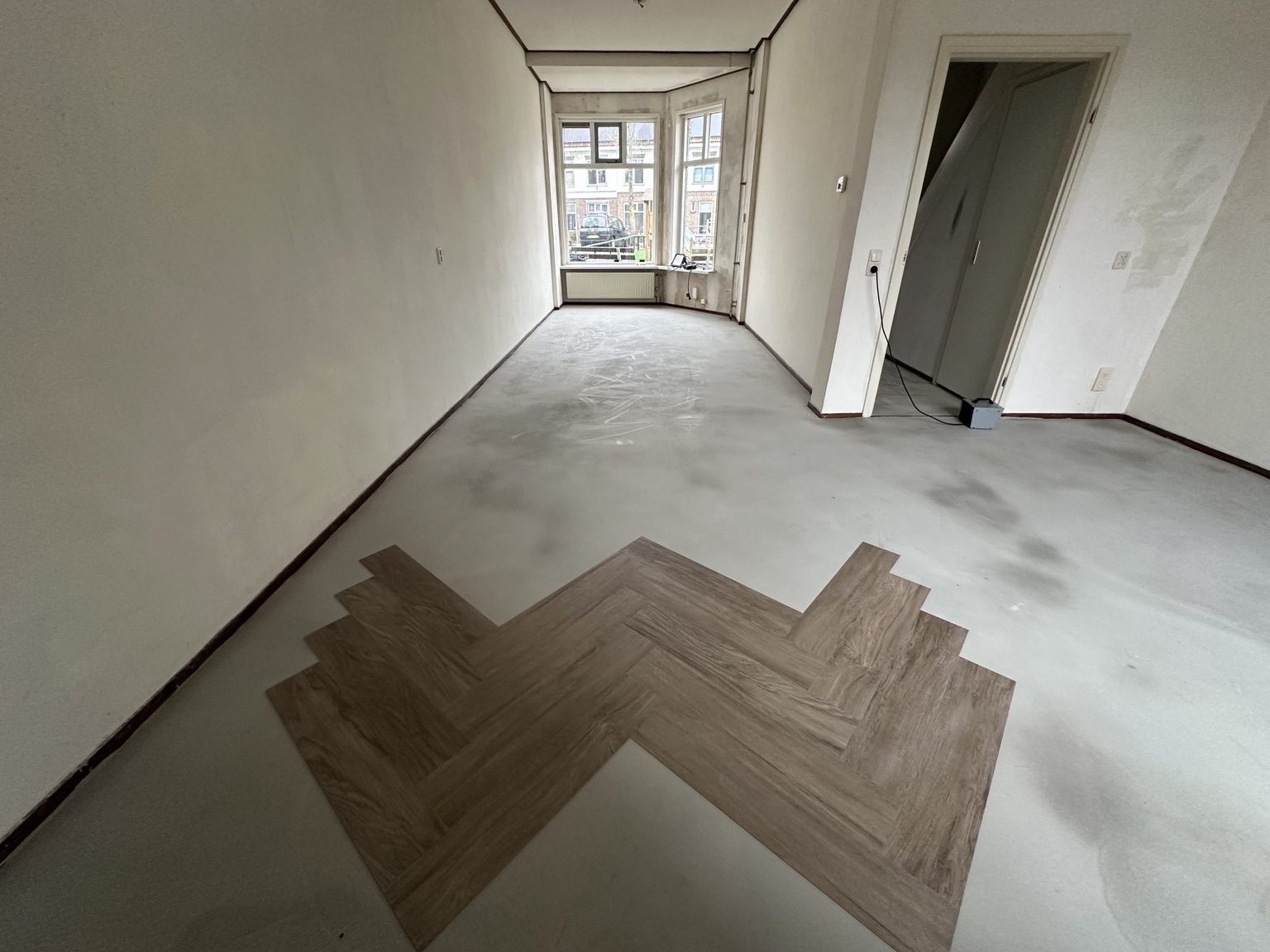 Start van de montage van plak-PVC in visgraatpatroon op de voorbereide ondervloer