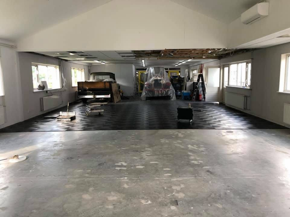 PVC-vloervak gemonteerd in de oldtimer-garage terwijl de rest van de vloer nog openligt en auto's blijven staan