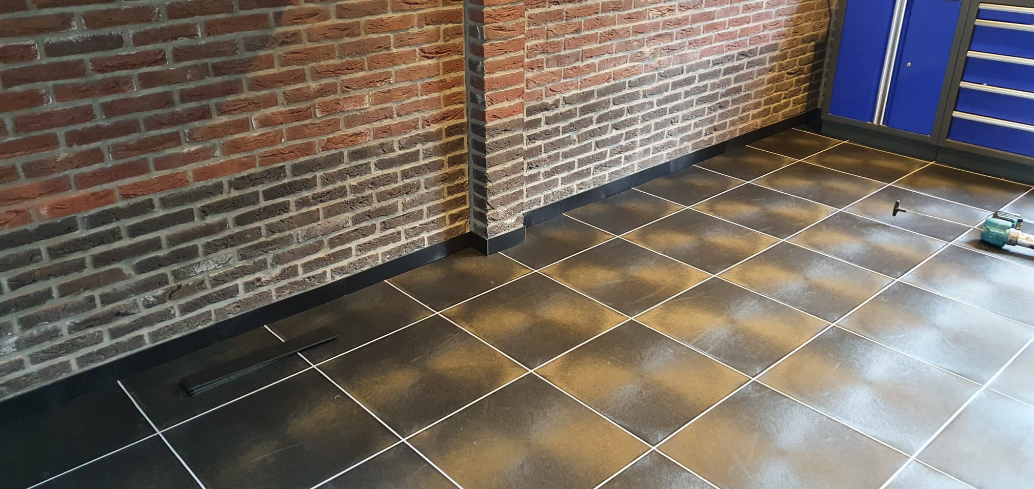 Detail van zwarte PVC-bedrijfsvloertegels met lichte voegen en zwarte plint in een particuliere garage
